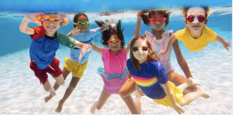 A group of smiling children swimming underwater in their goggles