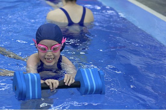 A smiling young swimmer in a lesson, with her instructor nearby